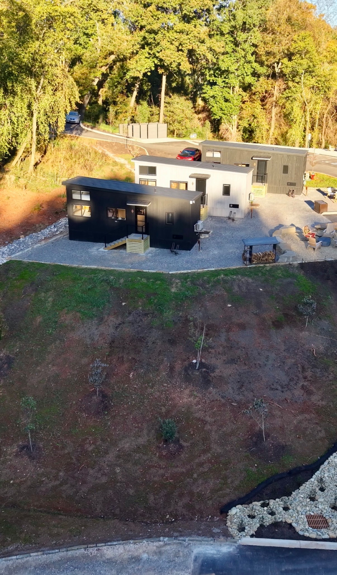 Aerial view of three modern cabins, a fire pit area and woods at The Drop Inn in Knoxville’s Urban Wilderness