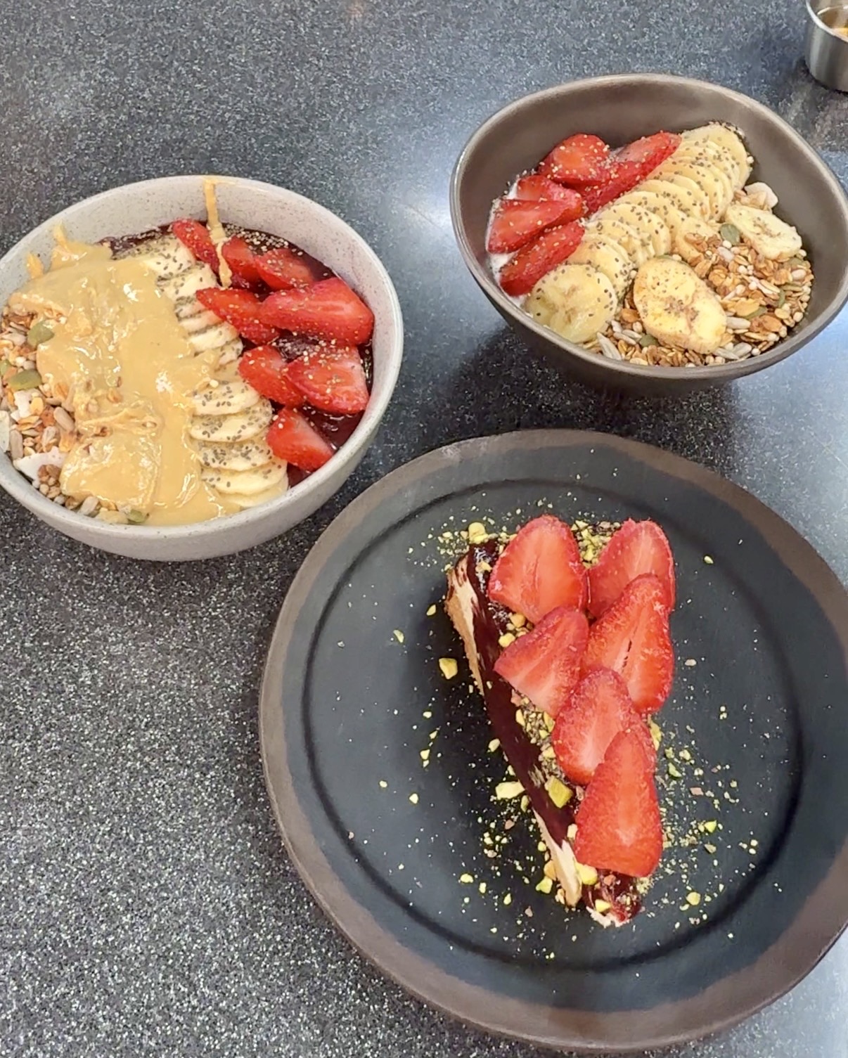 Smoothie bowls topped with strawberries, banana and peanut butter beside a slice of chocolate cake with strawberries