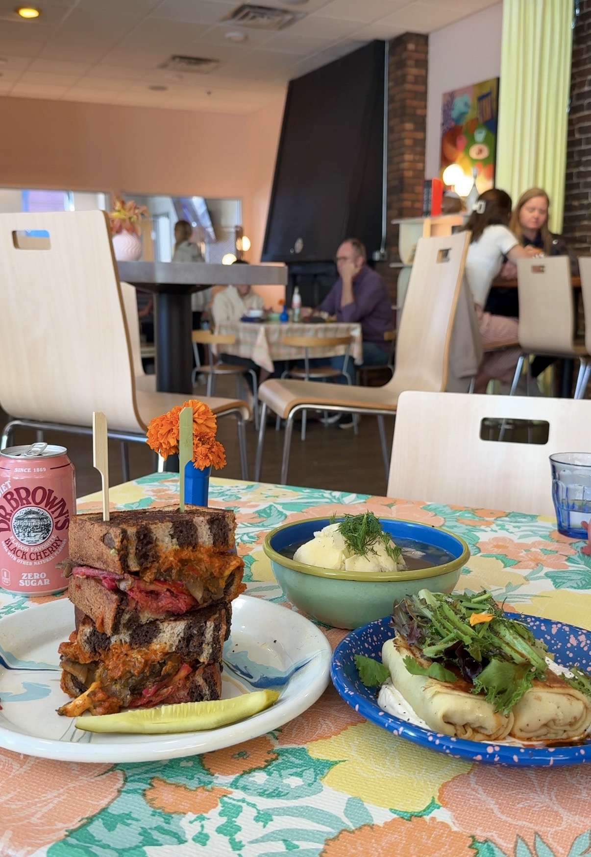 A stacked grilled sandwich on marbled rye, a bowl of soup and blintzes on a floral tablecloth at Potchke Deli in Knoxville